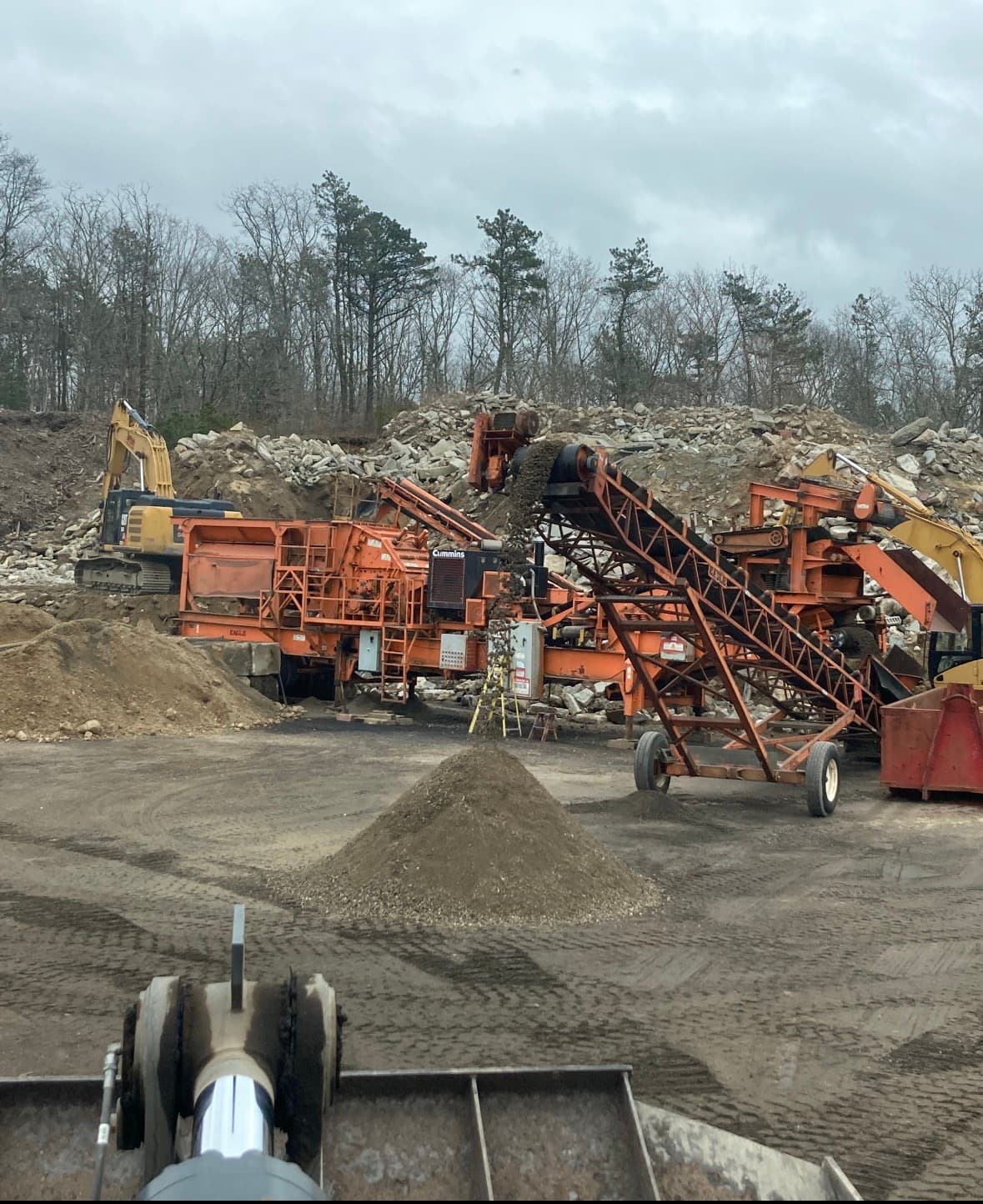 Orange rock crusher processing debris into a pile of gravel at a construction site.