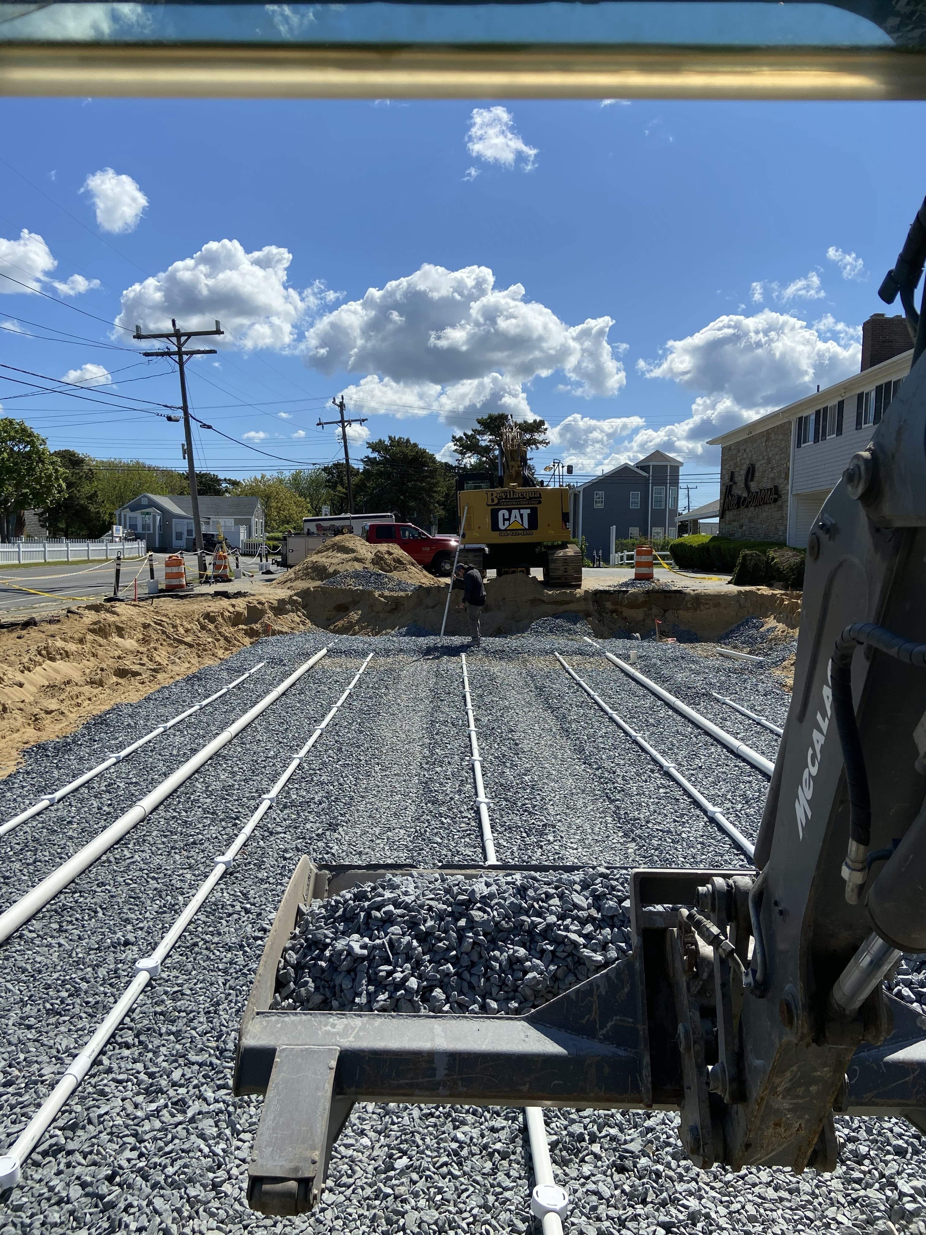 White pipes on grey gravel at a construction site with heavy machinery and blue sky.
