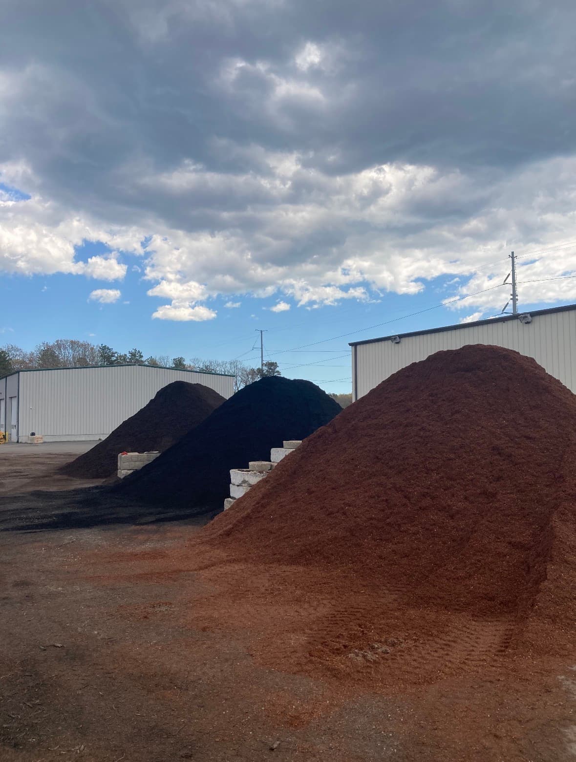 Large piles of red, black, and brown mulch in a yard under cloudy skies.